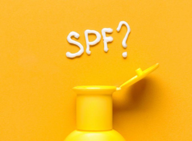 黃色背景上的防曬乳瓶與用乳液寫出的SPF問號，象徵防曬係數疑問